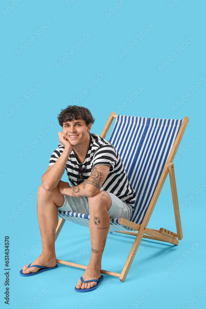 Young man sitting in deck chair on blue background