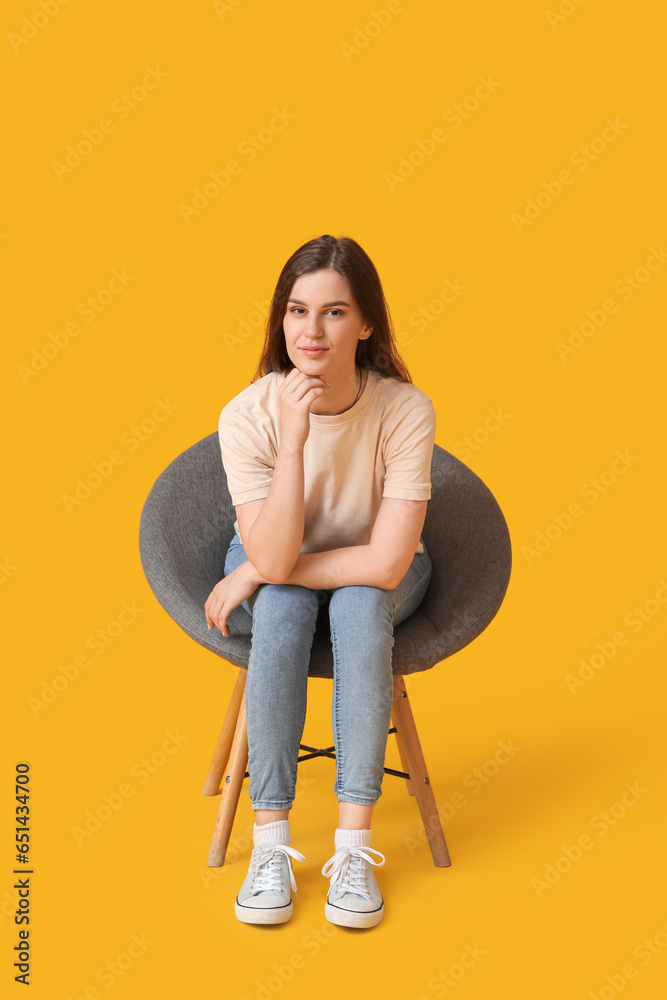 Young woman sitting in armchair on yellow background