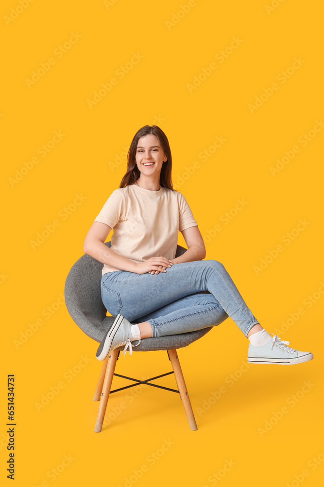 Young woman sitting in armchair on yellow background