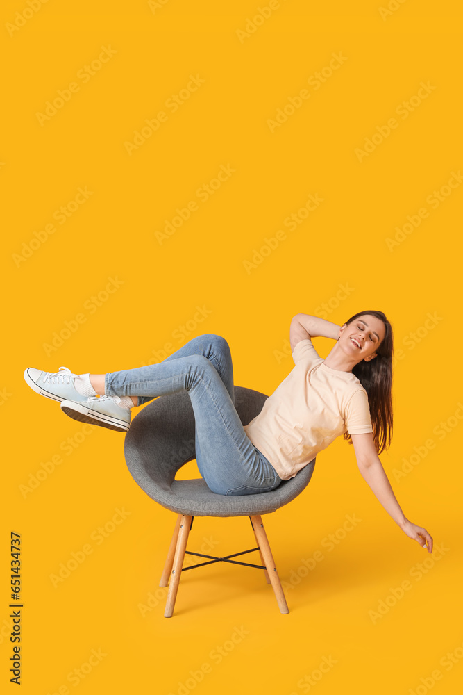 Young woman sitting in armchair on yellow background