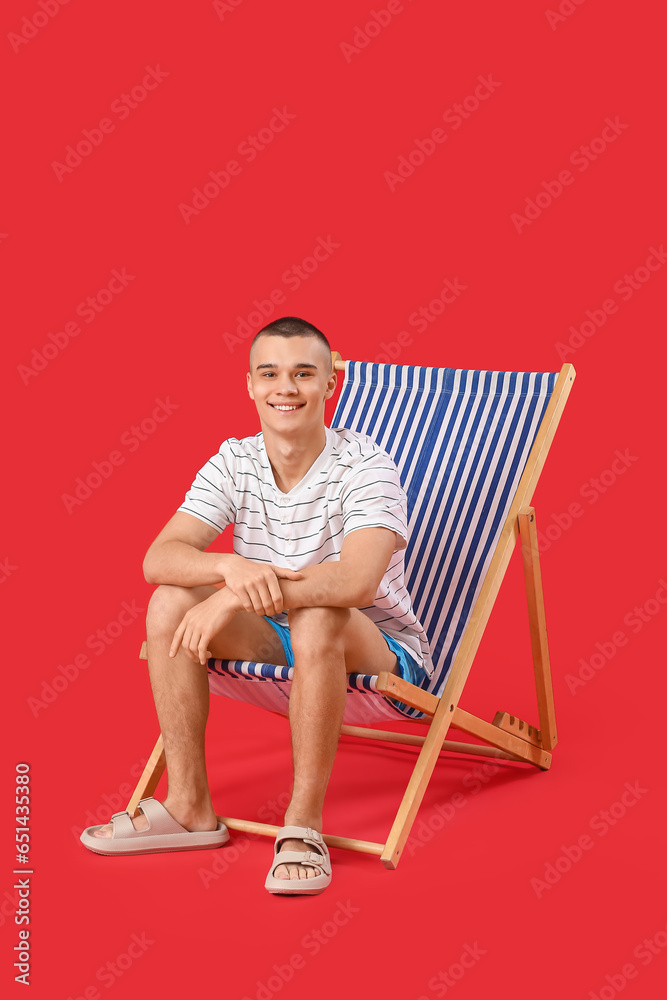 Happy young man sitting on deckchair against red background