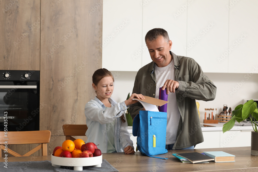 Father helping his little daughter to pack schoolbag in kitchen