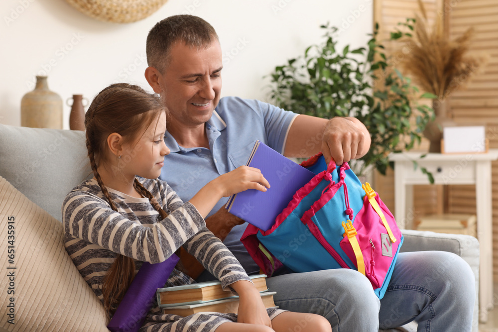 Father helping his little daughter to pack schoolbag at home