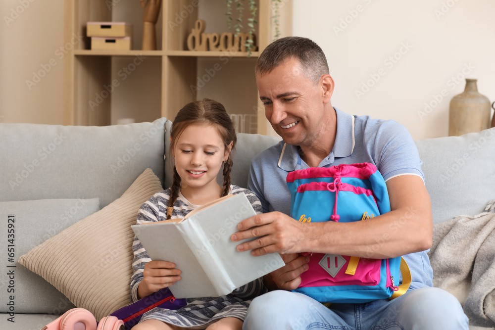 Father helping his little daughter to pack schoolbag at home