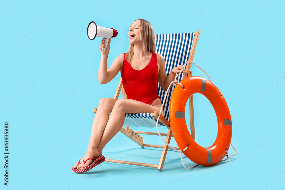 Beautiful woman with megaphone, deck chair and ring buoy on blue background