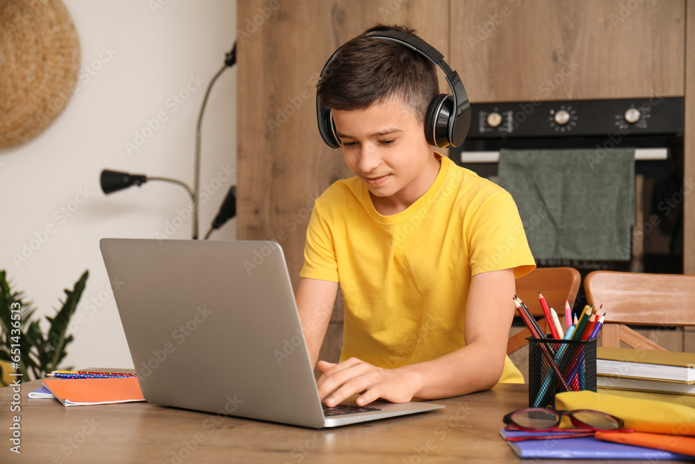 Little boy with headphones and laptop studying online in kitchen