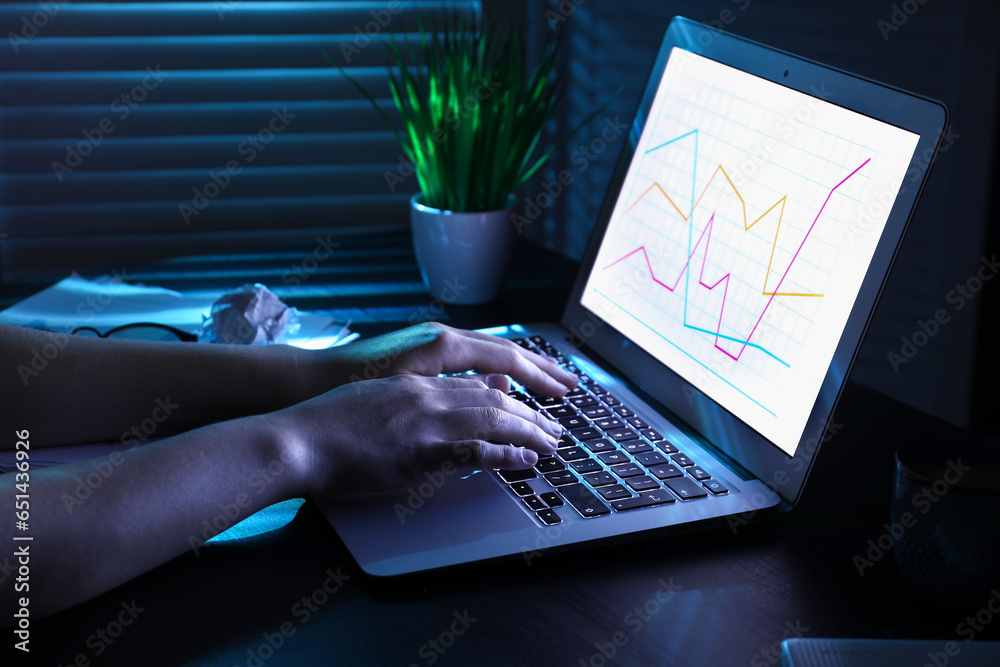 Female programmer typing on laptop keyboard at night in office, closeup