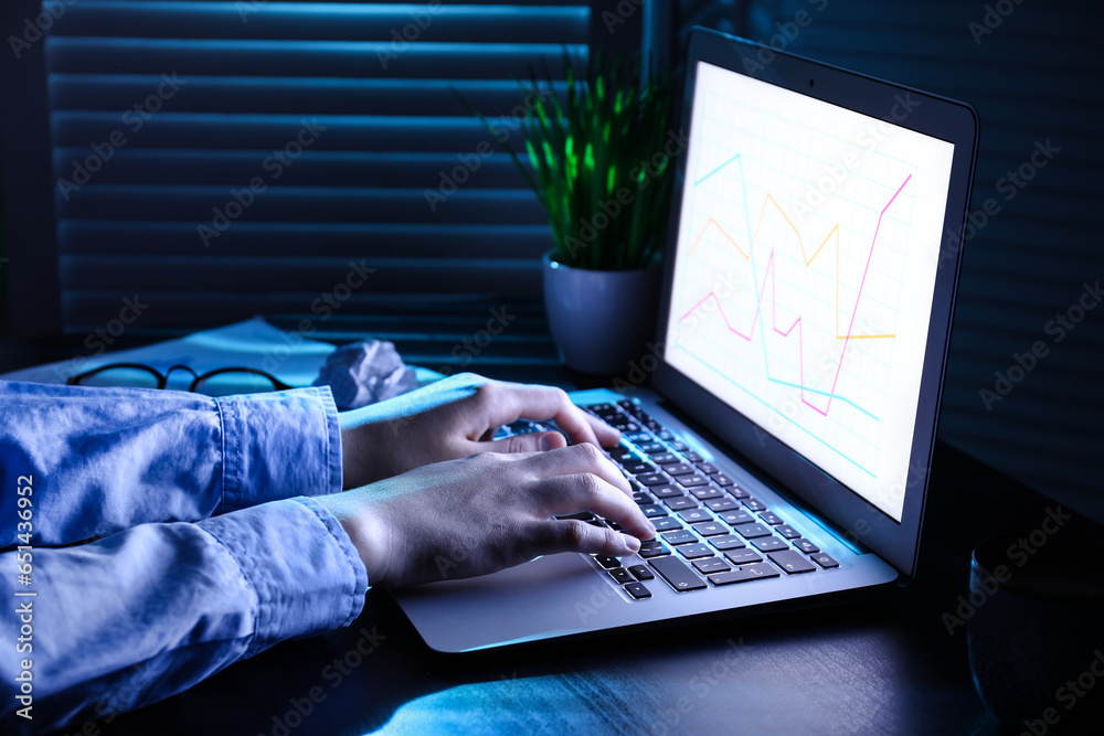 Female programmer typing on laptop keyboard at night in office, closeup