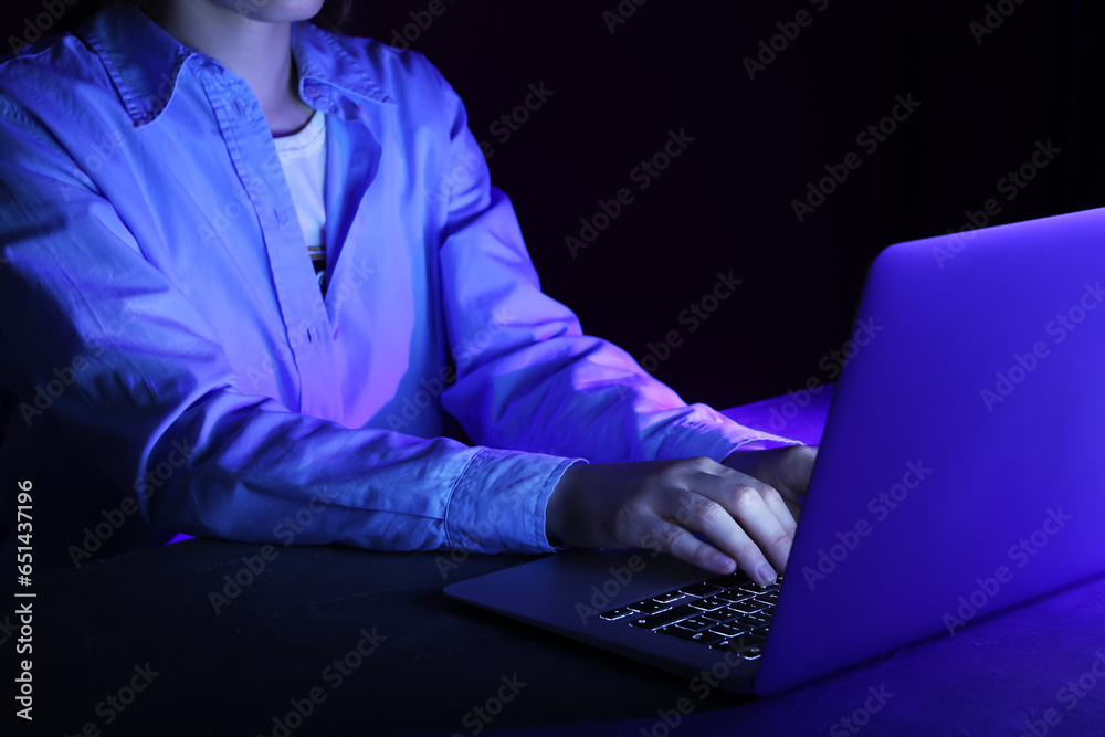 Female programmer typing on laptop keyboard at night in office, closeup