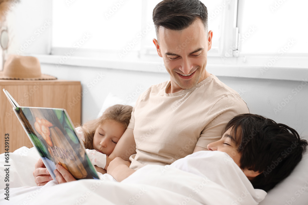 Father reading story to his little children in bedroom