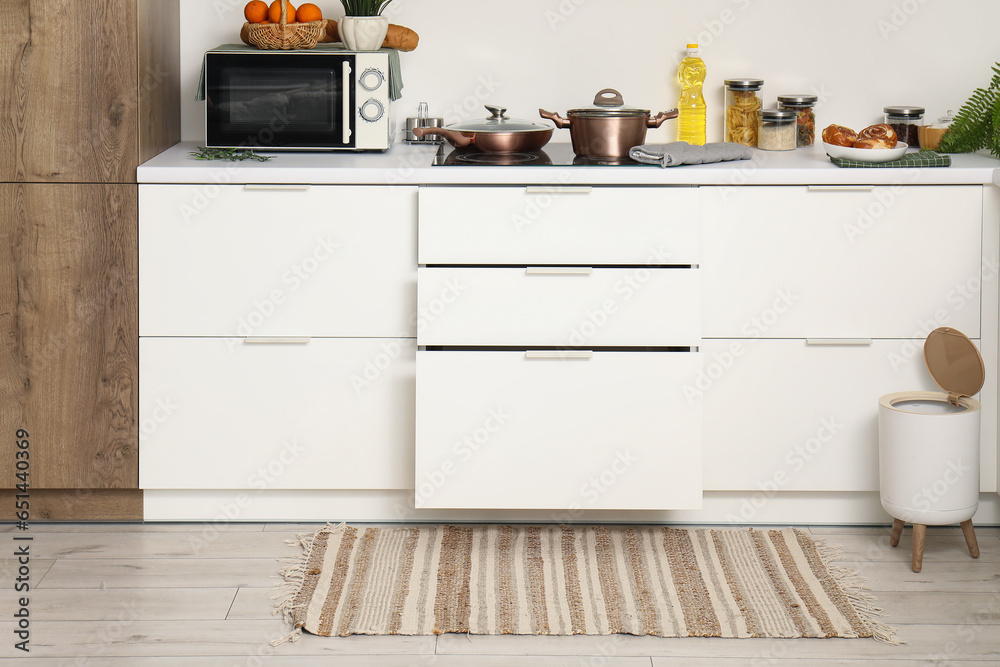 Interior of modern kitchen with stylish rug, trash bin and white counters