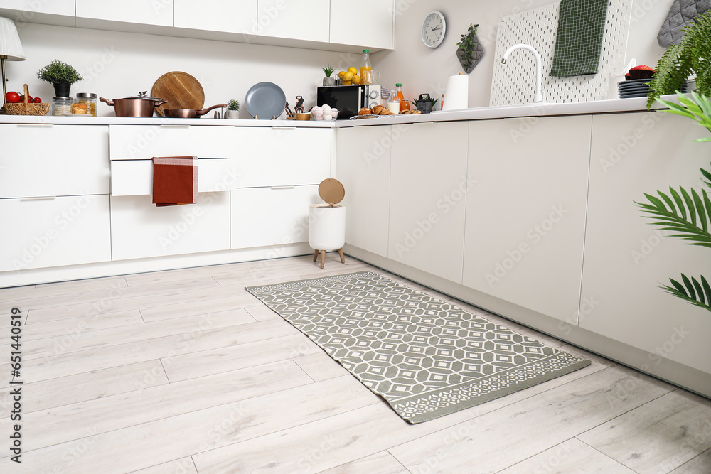 Interior of modern kitchen with stylish rug, trash bin and white counters