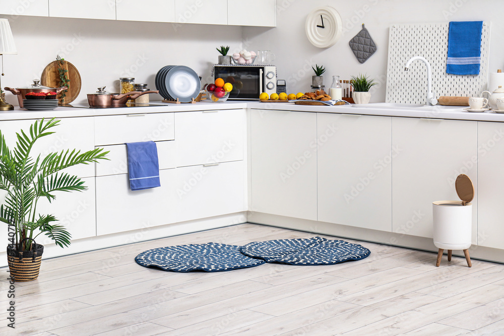 Interior of modern kitchen with stylish rugs, trash bin and white counters