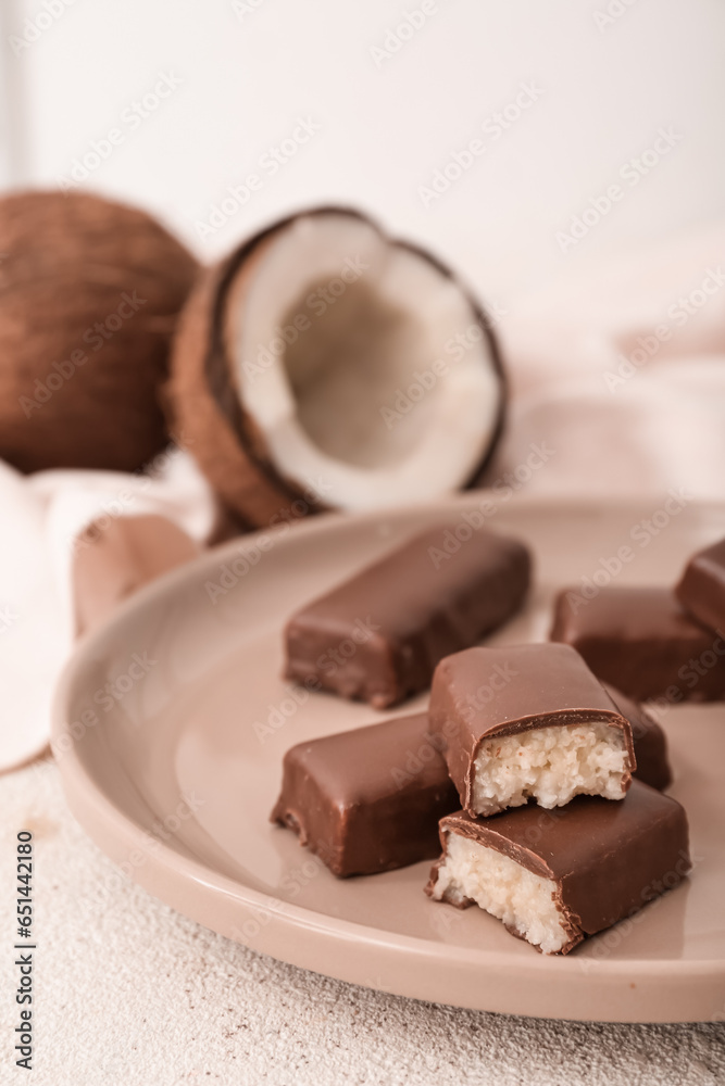 Plate with tasty chocolate covered coconut candies on light background