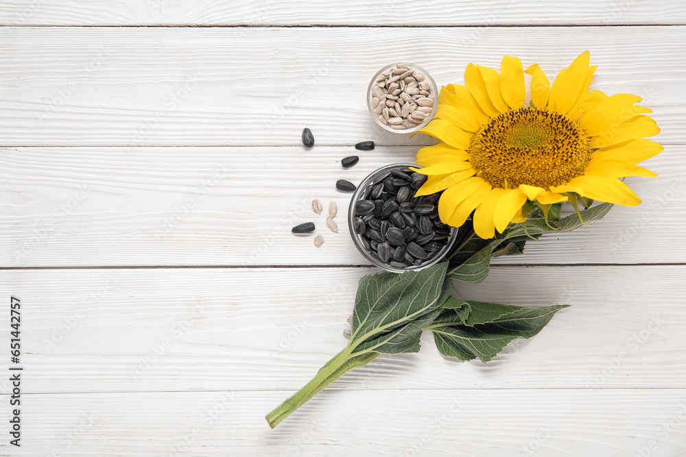 Beautiful sunflower and bowls with seeds on white wooden background