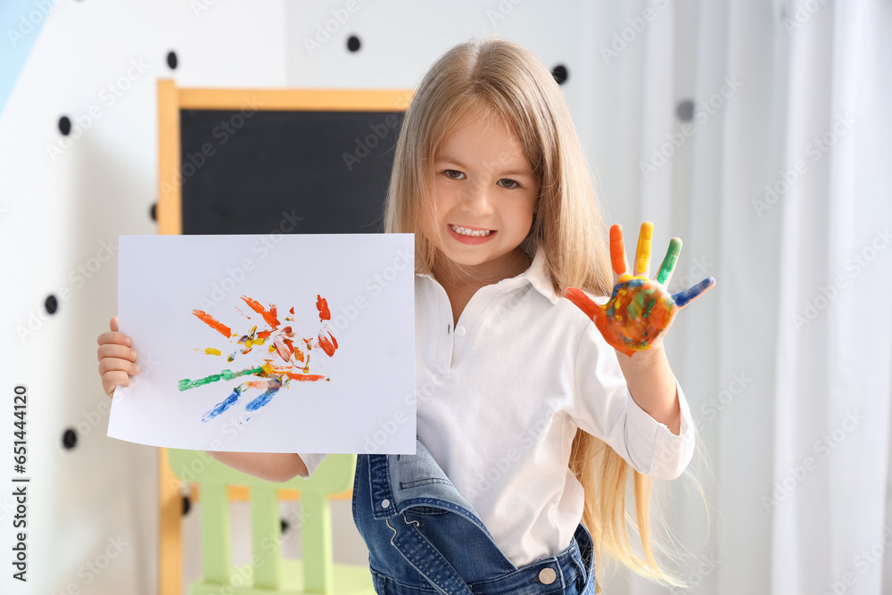 Cute little girl with her hand in paint and drawing at home