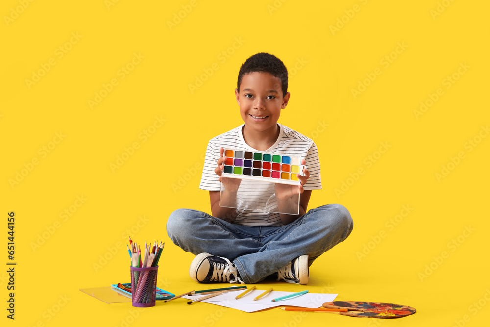 Little African-American boy with paints on yellow background