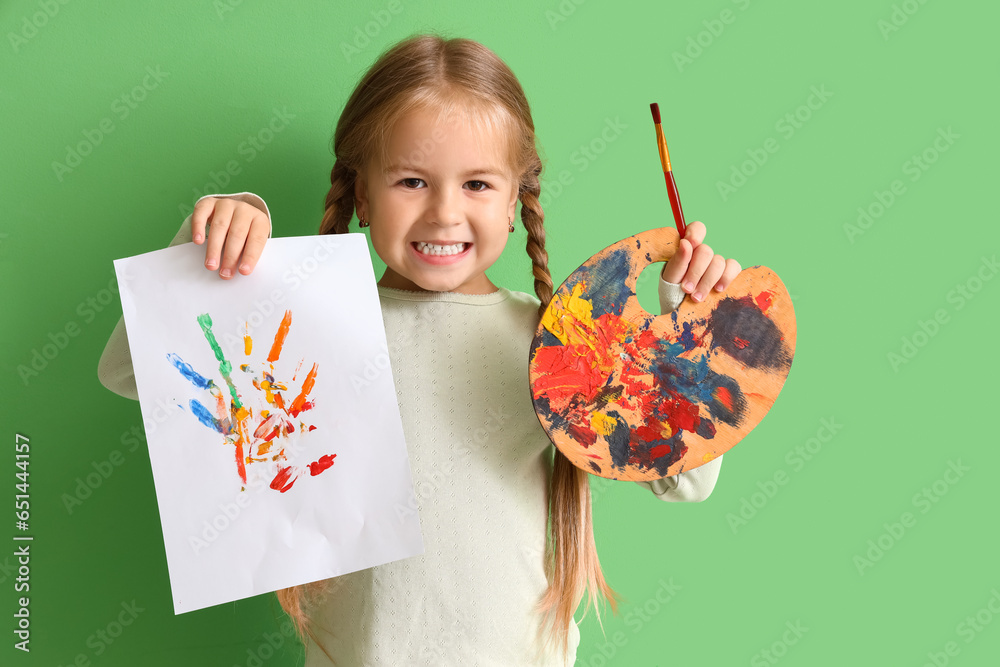 Cute little girl with drawing, paint palette and brush on green background