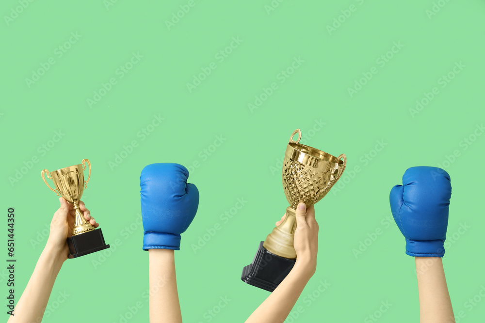 Female hands with gold cups and boxing gloves on green background