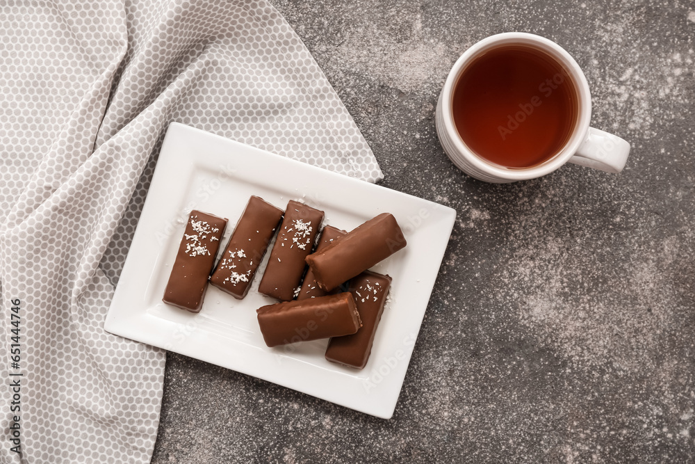 Plate with tasty chocolate covered coconut candies and cup of tea on grey background