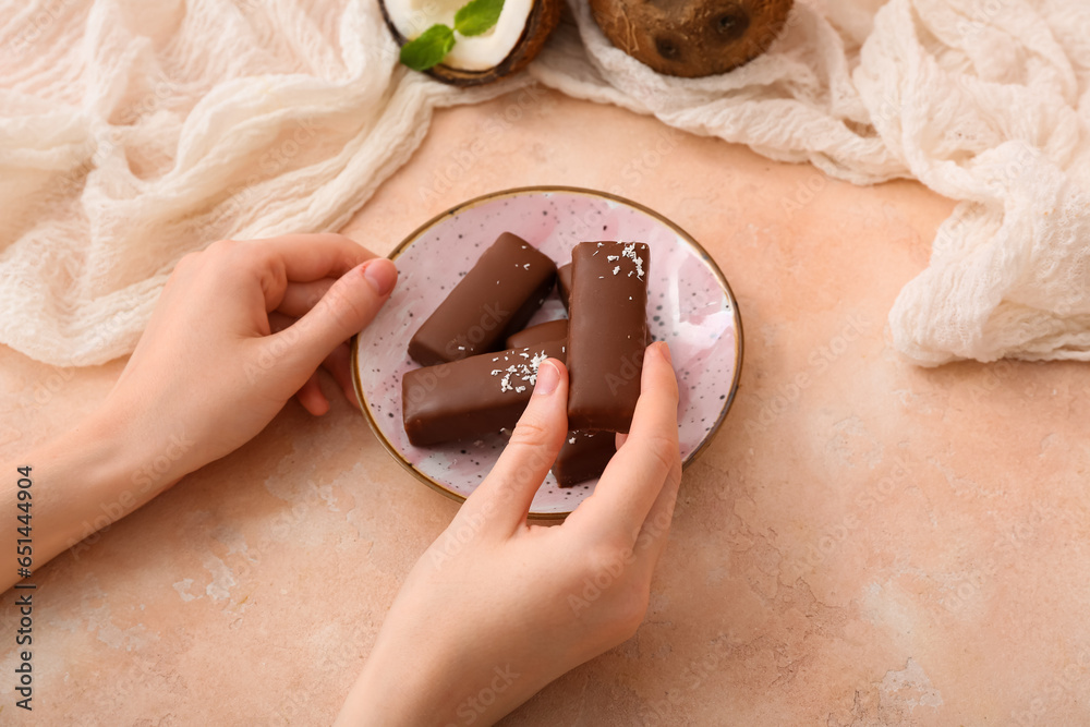 Woman eating tasty chocolate covered coconut candies on beige background