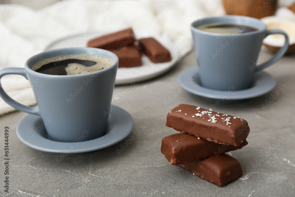 Tasty chocolate covered coconut candies and cups of coffee on grey background