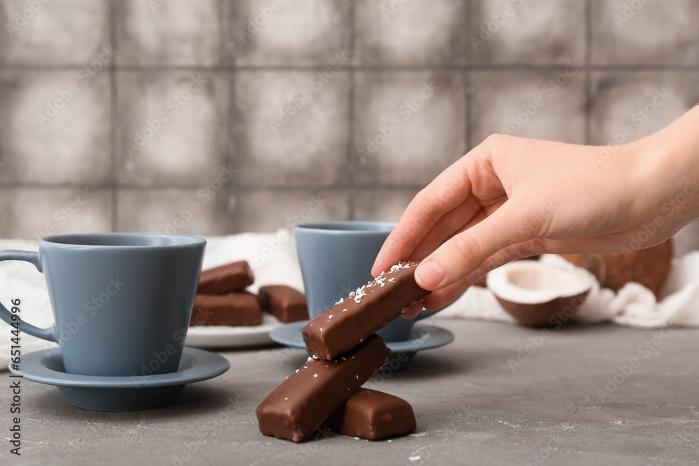 Woman eating tasty chocolate covered coconut candies at table