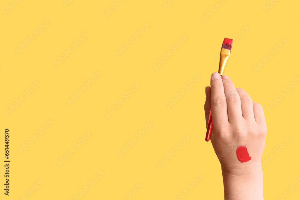 Female hand with artists brush on yellow background