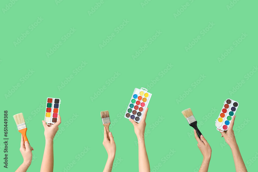 Female hands with artists supplies on green background