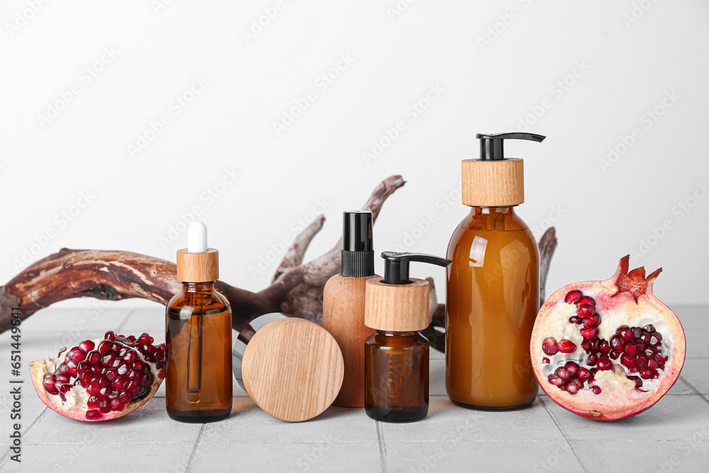 Composition with different cosmetic products, pomegranate and tree branch on table against light background