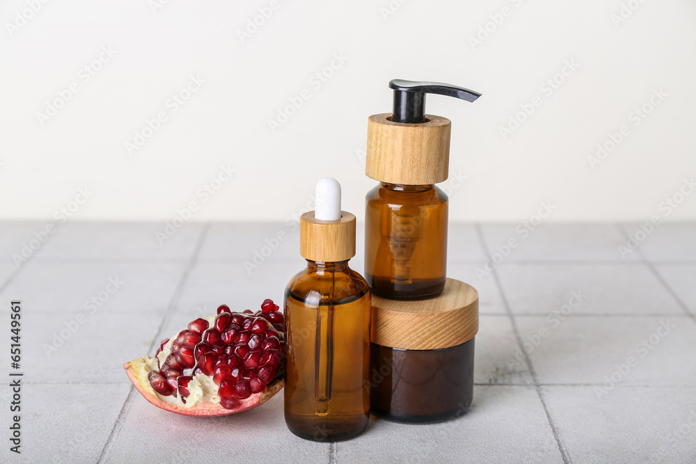 Set of cosmetic products and pomegranate on tile table against light background