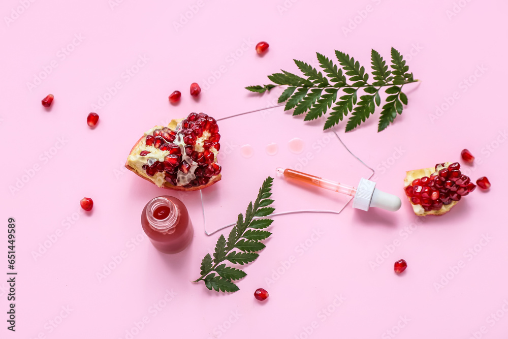 Composition with bottle of essential oil, pomegranate and fern leaves on pink background