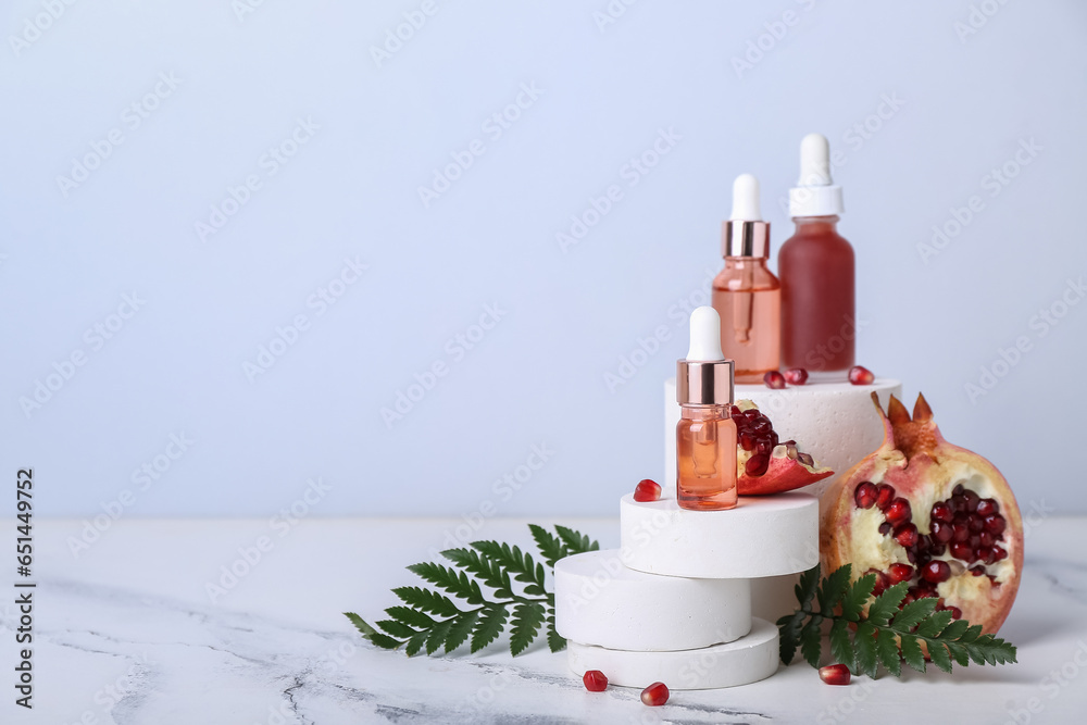 Composition with bottles of essential oil, pomegranate and fern leaves on light background