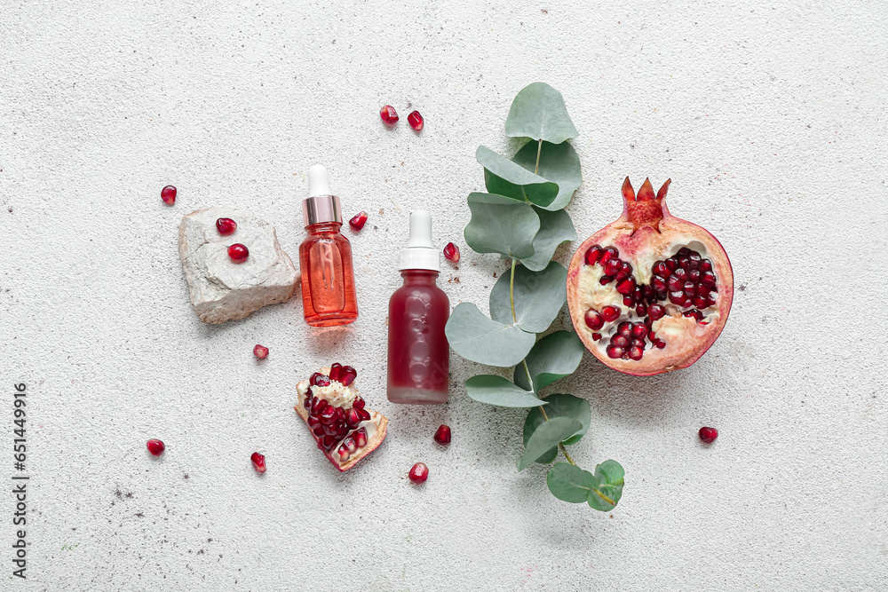 Composition with bottles of essential oil, pomegranate and eucalyptus branch on light background