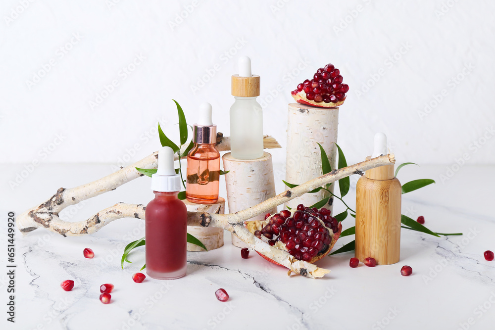 Composition with bottles of essential oil, tree branch and pomegranate on light background