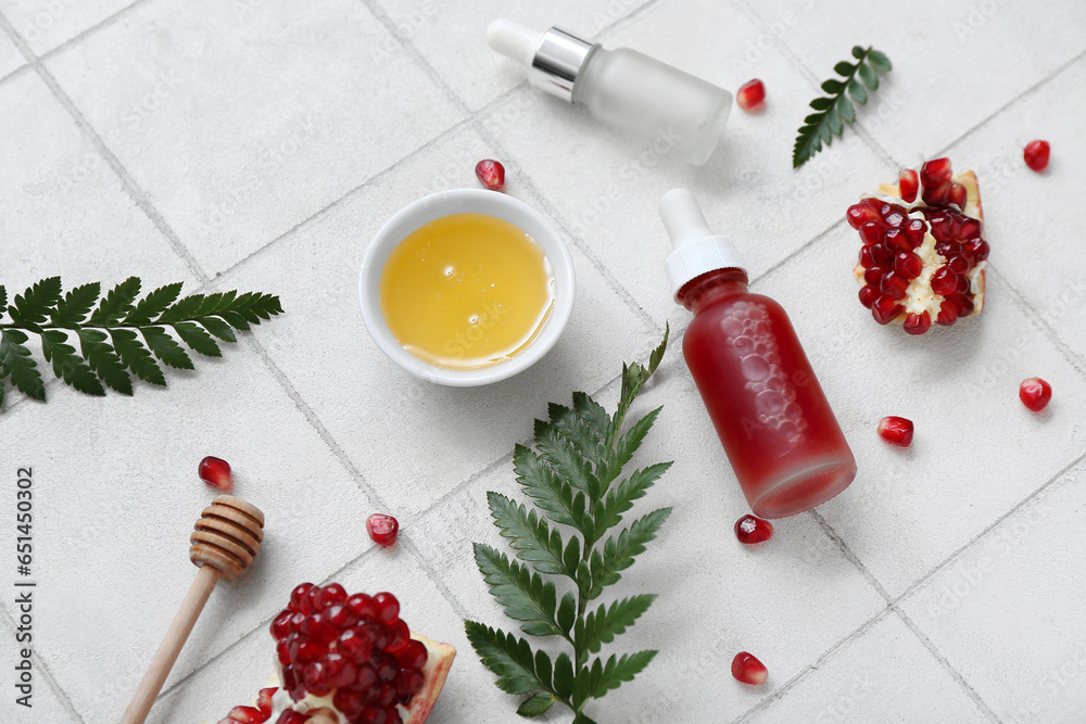 Composition with bottles of essential oil, honey, pomegranate and fern leaves on light tile background