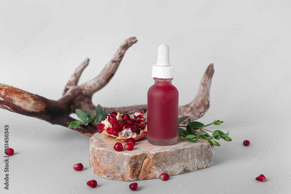 Composition with bottle of essential oil, pomegranate and tree branch on light background