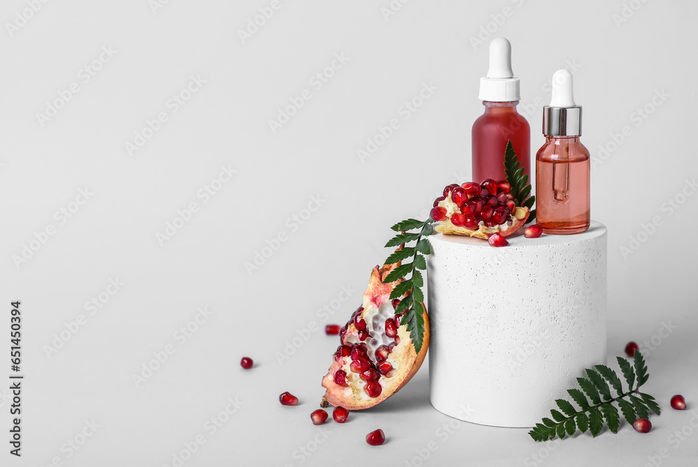 Composition with bottles of essential oil, plaster podium and pomegranate on light background