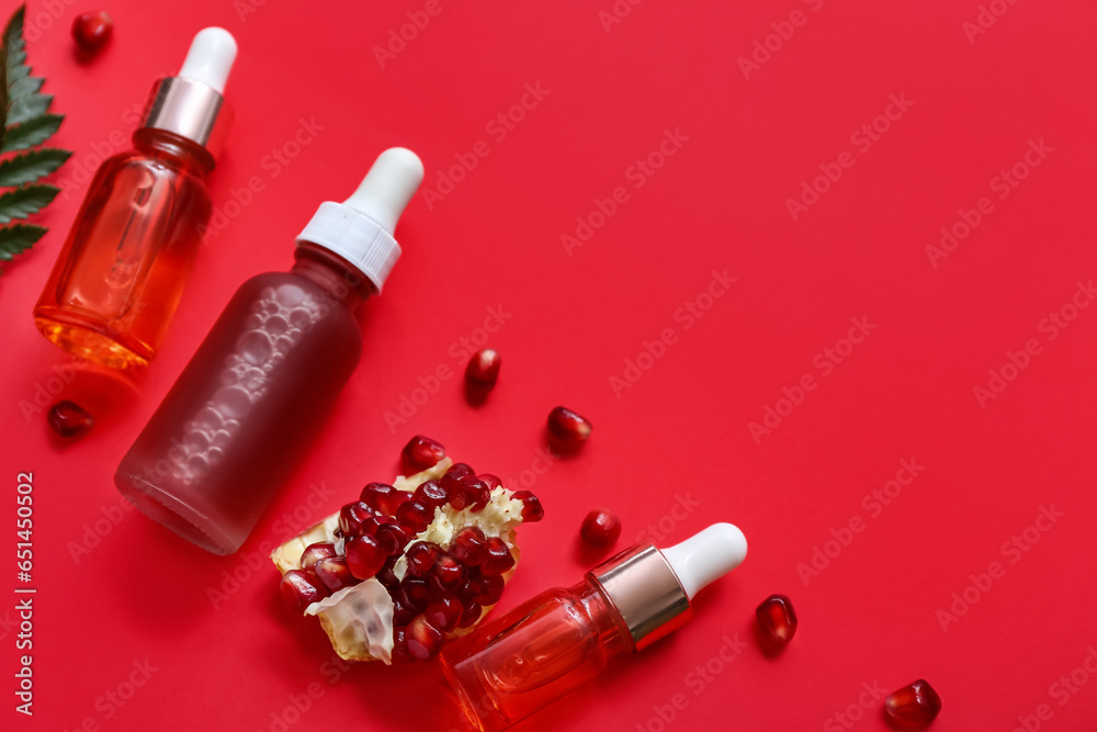 Composition with bottles of essential oil and pomegranate on red background