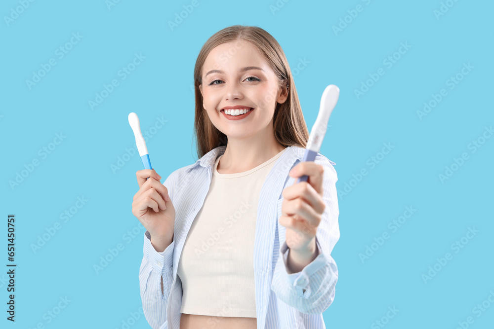 Happy young woman with positive pregnancy tests on blue background