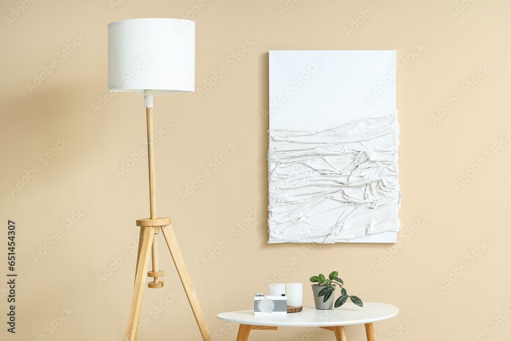 Painting, small table and standard lamp near beige wall