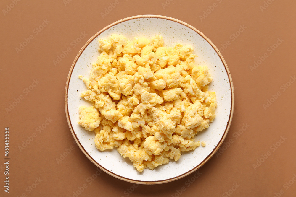 Plate of tasty scrambled eggs on brown background