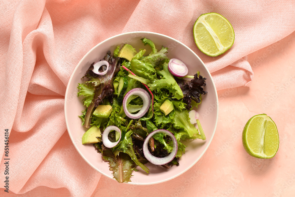 Bowl with fresh vegetable salad and lime on pink background