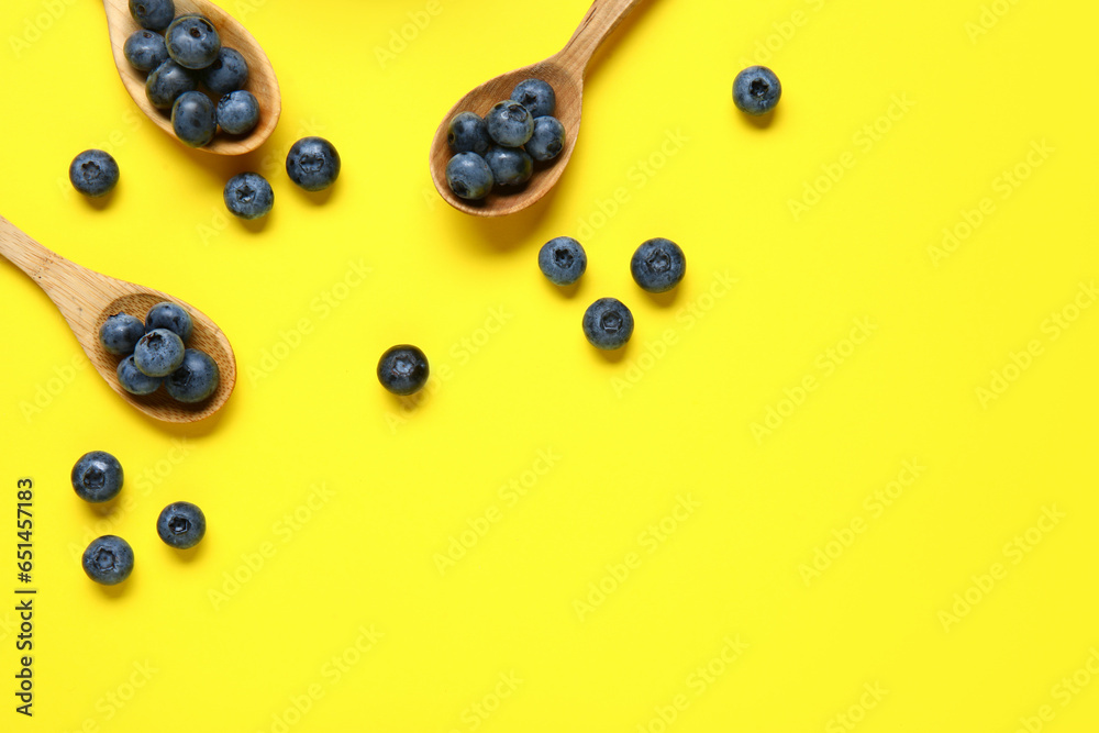 Wooden spoons with fresh blueberries on yellow background