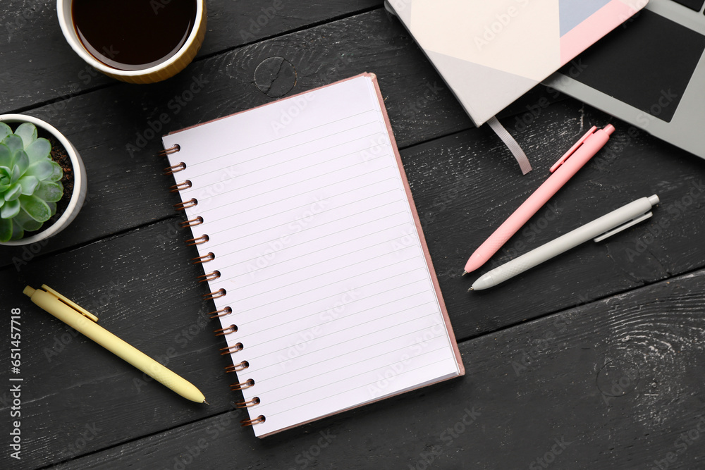 Notebooks with pens and cup of tasty coffee on black wooden background