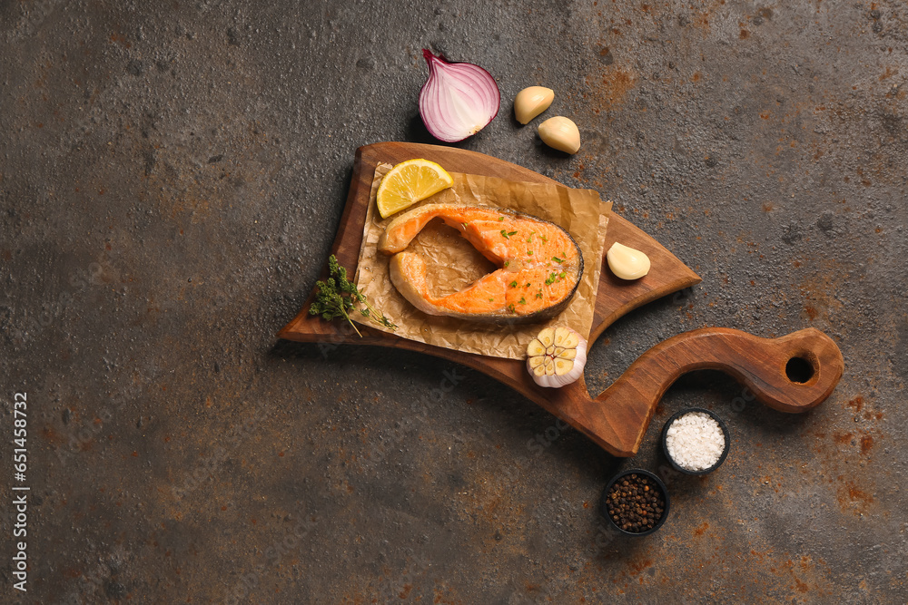 Wooden board of tasty salmon steak with garlic, onion and lemon on brown background