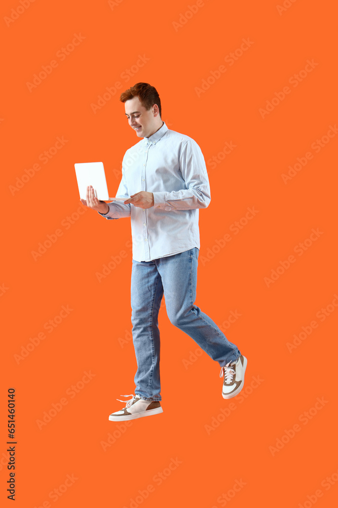 Jumping young man with laptop on orange background