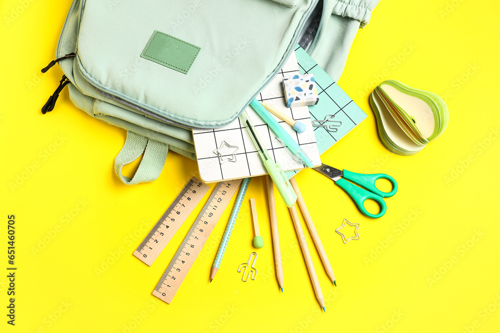 Stylish school backpack with different stationery supplies on yellow background