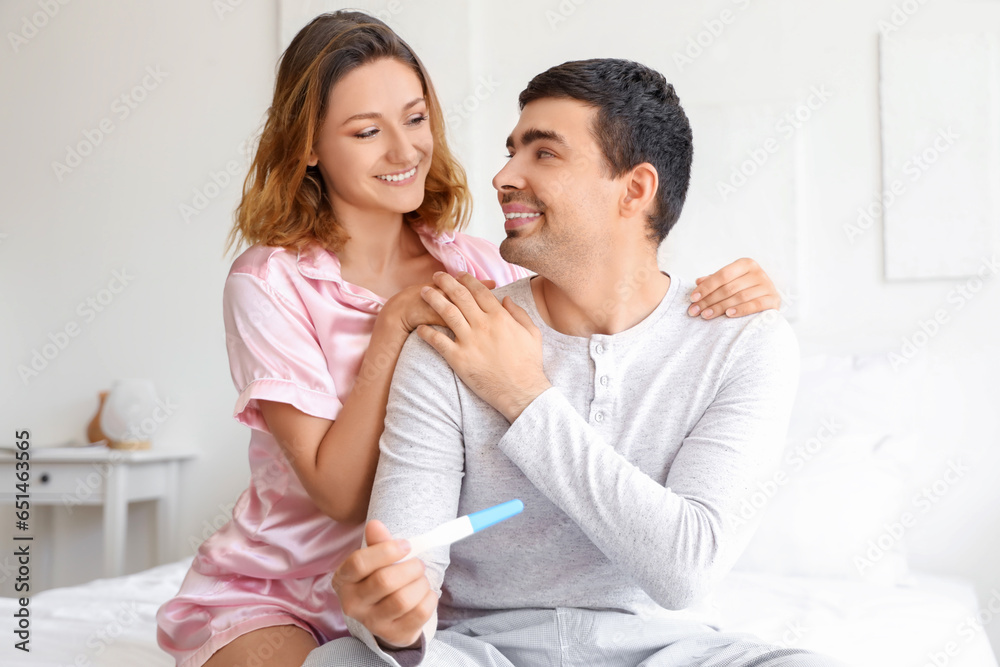 Happy young couple with pregnancy test in bedroom