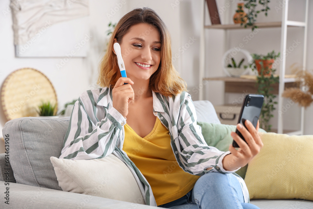 Happy young woman with pregnancy test taking selfie at home